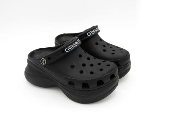 A pair of black crocs on top of a white surface.